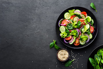 Salade de légumes sains de tomate fraîche, concombre, oignon, épinards, laitue et sésame sur assiette. Menu diététique. Vue de dessus.