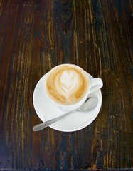 Flat white coffee, similar to a cafe latte with pattern in the foam on a dark timber table background