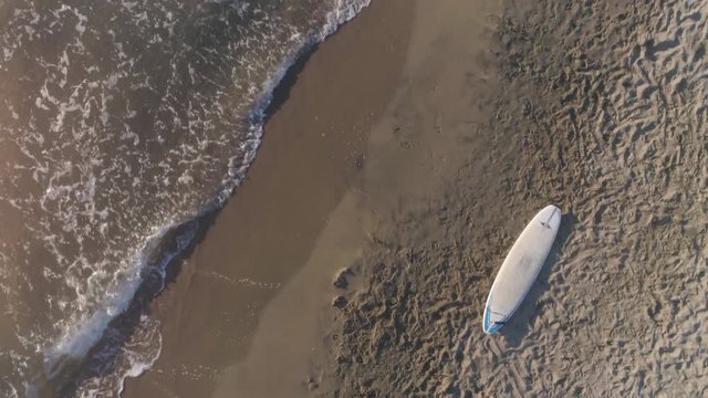 Aerial top view of surf board lying down on the sand at the beach at sunset