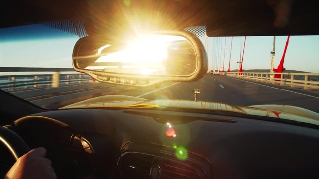 Cabriolet is driving along Russian bridge (connects the mainland part of Vladivostok with Russian Island), middle aged driver's portrait in sunglasses. Sunrise