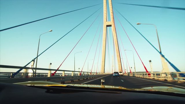 Cabriolet is driving along Russian bridge (connects the mainland part of Vladivostok with Russian Island), middle aged driver's portrait in sunglasses. Sunrise