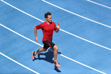 Sprinter man running on blue tracks lanes in track and field stadium in high speed top view. Male...