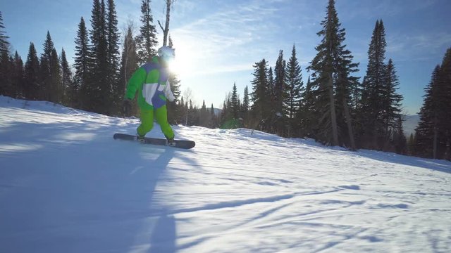 Sportsman snowboarder in bright clothes rides down the peak of a hill at winter sunny day