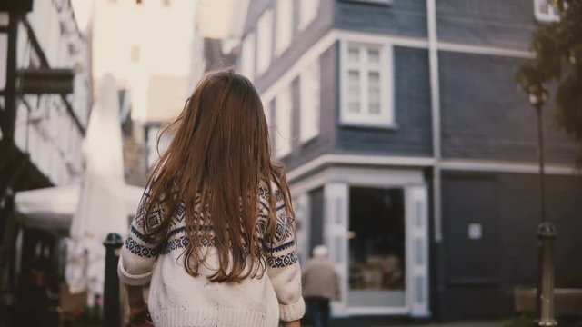 Camera follows little girl walking in old town. Back view. Female kid, long hair, wandering around ancient streets. 4K.