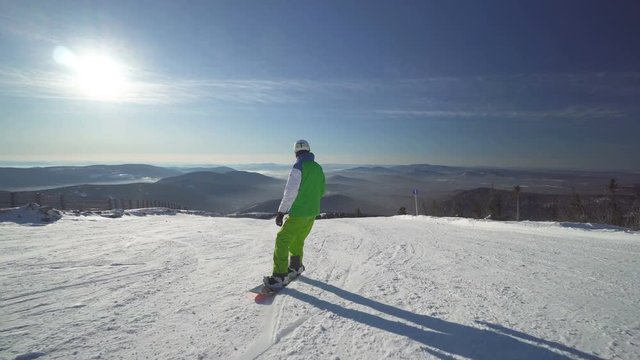 Sportsman snowboarder in bright clothes is riding down fastly on the slope of a hill at winter sunny day