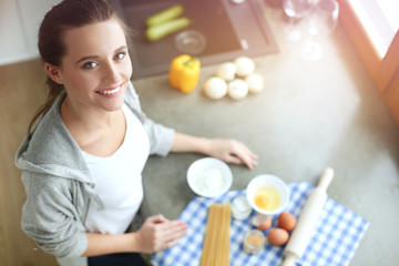 Beautiful woman cooking cake in kitchen standing near desk.