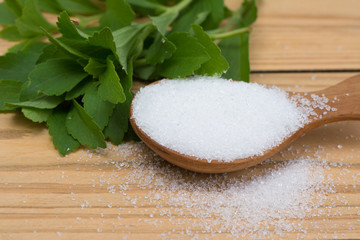 fresh stevia leaves and sugar in wooden spoon on wooden background