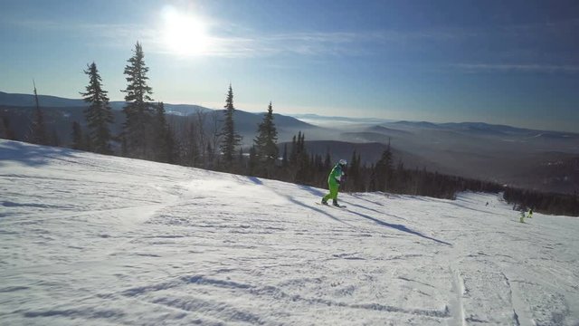Snowboarder in bright green clothes rides down fastly on the slope of a mountain at winter sunny day