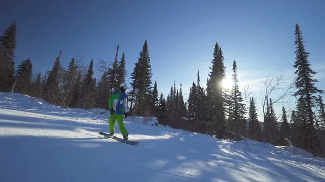 Snowboarder in bright green clothes rides down fastly on a slope of the mountain at winter sunny day