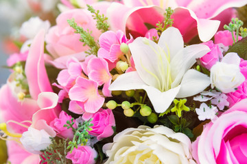 Close up to colorful plastic pink lilly flowers with roses and little flowers in a bouquet.