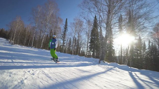 Snowboarder sportsman in bright green clothes rides down fastly on a slope of the mountain at sunny winter day