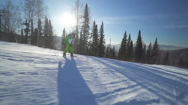 Sportsman on board in bright green clothes is riding down fastly upon a slope of the hill at sunny winter day