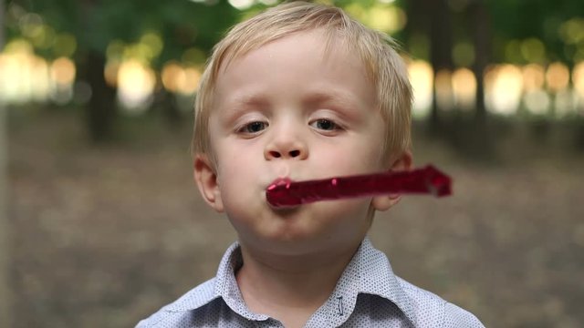 Happy little boy are blowing into unfolding tube at a birthday party. Little boy having fun and blows a party horn. Little boy with birthday pipes.