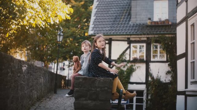 Caucasian boy and girl sit together, side view. Siblings on a sunny day. Ancient half-timbered houses. 4K.
