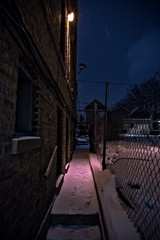 Dark and scary urban city gangway during the winter with snow and foot prints by a vintage brick...