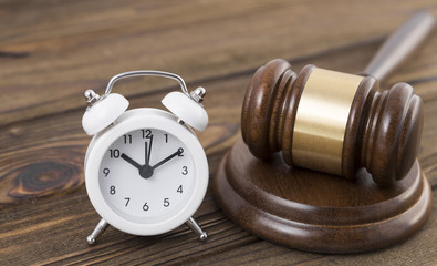 Alarm clock, judge hammer against the background of a wooden table. Time of the meeting. Justice.