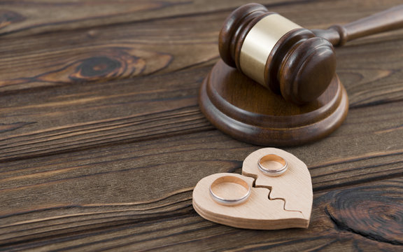 Wedding rings on the figure of a broken heart from a tree, hammer of a judge on a wooden background. Divorce divorce proceedings