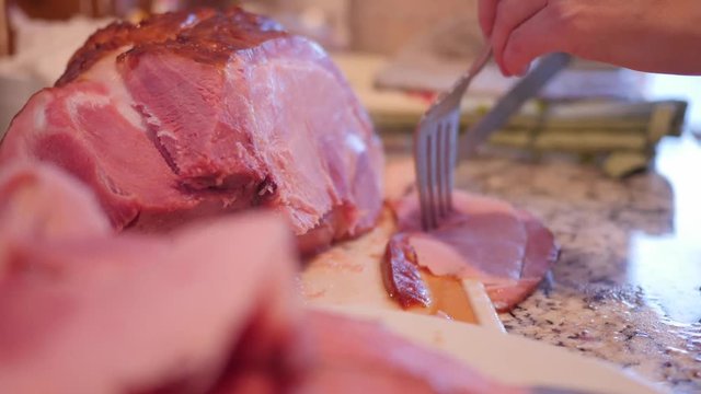 A dolly shot as woman cuts up a holiday ham for dinner