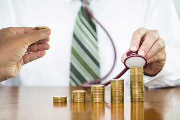 Businessman hand holding stethoscope checking stack of coins arranged as a graph with man hand holding putting on stack of money coin, concept of financial health check and saving money