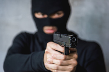 Masked robber with gun aiming