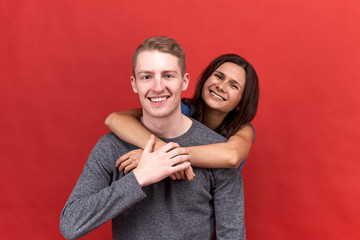 Happy beautiful couple smiling widely at the camera showing white teeth. Lovers hugging in the isolated red background.