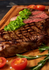 Grilled Black Angus Steak with tomatoes, garlic with chimichurri sauce on meat cutting board.