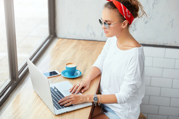 Indoor shot of successful young female enterpreneur visits web page, works online as creats business project, keyboards text message, sits at cafe. Fashionable blogger makes personal website