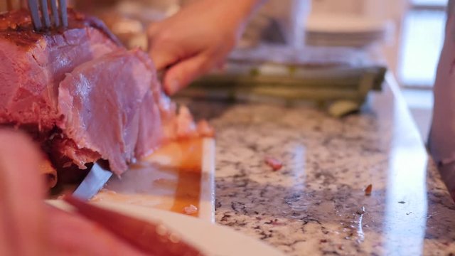 Dolly shot as woman cuts up a holiday ham for dinner