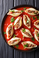Italian cuisine: conchiglioni pasta stuffed with ground beef with greens in tomato sauce close-up on plate. Vertical top view