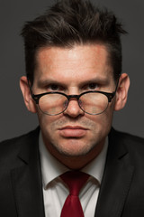 Close-up portrait of serious angry businessman in formal costume and wearing glasses on gray background