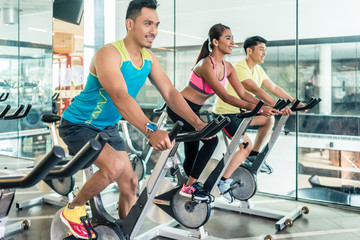 Fototapeta na wymiar handsome and confident young man smiling while pedaling during group class of HIIT indoor cycling in a modern fitness club