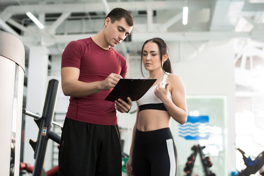 Portrait of young woman signing contract with personal fitness coach in modern gym, copy space