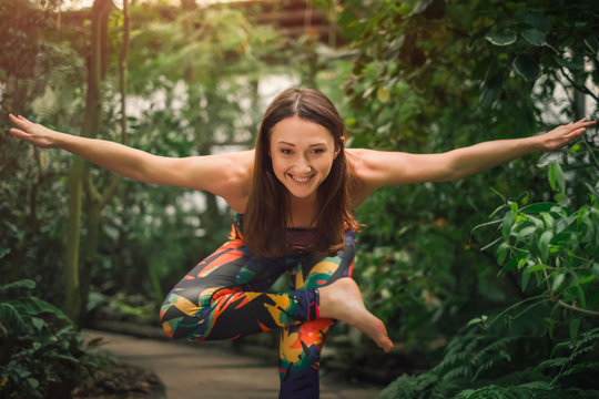 Happy young woman doing yoga exercises for balance at greenhouse