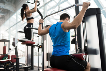 Fototapeta na wymiar Side view of two people exercising on machines in modern gym by window