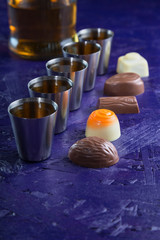 set of five servings of cognac with a variety of chocolates on a dark purple background