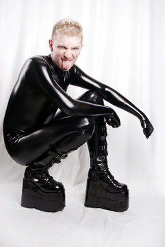 trendy guy dressed in a tight latex suit and platform boots posing in Studio on white background alone