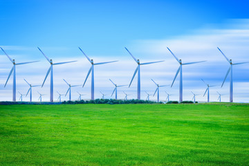 Wind turbines generating electricity on green meadow at daytime.