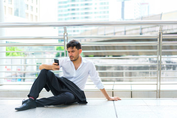 Handsome businessman sitting outdoors and holding smartphone. concept of relax, feeling, technology and attractive.