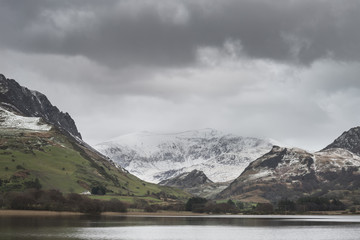 Fototapeta na wymiar Beautiful Winter landscape image of Llyn Nantlle in Snowdonia National Park with snow capped mountains in background