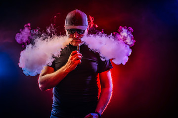vaping man holding a mod. A cloud of vapor. Black background. vaping man holding a mod. A cloud of...