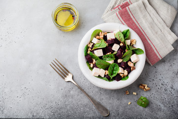 Chard, arugula, beetroot, ricotta cheese and walnut salad with olive oil in a ceramic old plate on a gray stone or concrete aged background. Selective focus. Top view. Copy space.