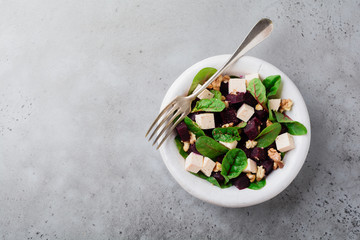 Chard, arugula, beetroot, ricotta cheese and walnut salad with olive oil in a ceramic old plate on a gray stone or concrete aged background. Selective focus. Top view. Copy space.