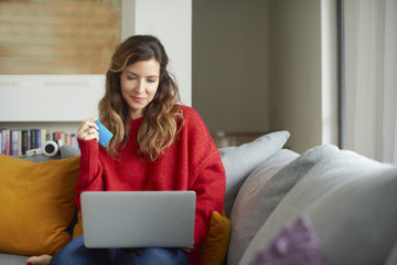 Shopping from my cosy sofa. Portrait of an attractive mature woman holding her bank card while sitting with her laptop on the sofa at home. 