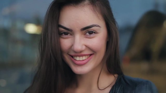 Beautiful girl smile and give air kiss in the evening. A brunette woman in a black leather jacket.