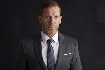 Confident middle aged businessman. Portrait shot of a middle aged businessman wearing suit and looking thoughfully while standing at dark background. Copy space. 