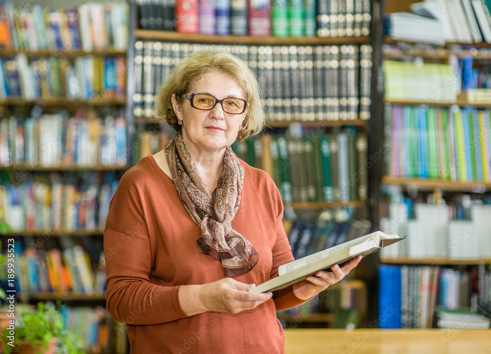 Wall mural elderly woman reading a book in the library