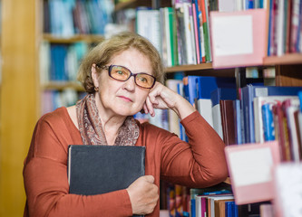 thoughtful elderly woman standing with book in library