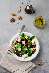 Chard, arugula, beetroot, ricotta cheese and walnut salad with olive oil in a ceramic old plate on a gray stone or concrete aged background. Selective focus. Top view. Copy space.