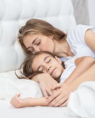 Mom and daughter sleep together on the bed in the bedroom