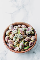 Pistachios in wooden bowl on marble background with copy space 